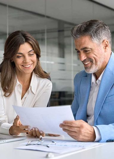 Outsourced DPO Services Two professionals, a man and a woman, smile while reviewing documents together.